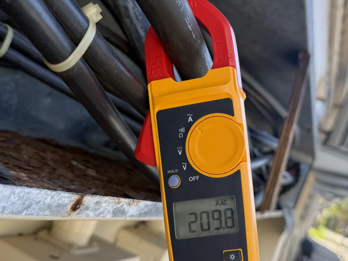 Clamp meter measuring 209.8 amps on outdoor electrical service conductors