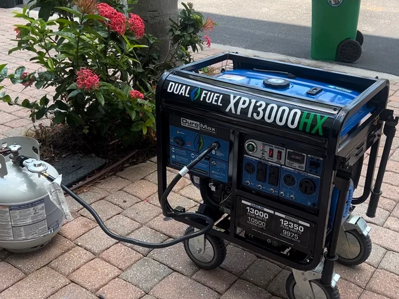 Dual-fuel portable generator on a paver driveway with its fuel line run to a propane tank — backup power set up by Far Out Design