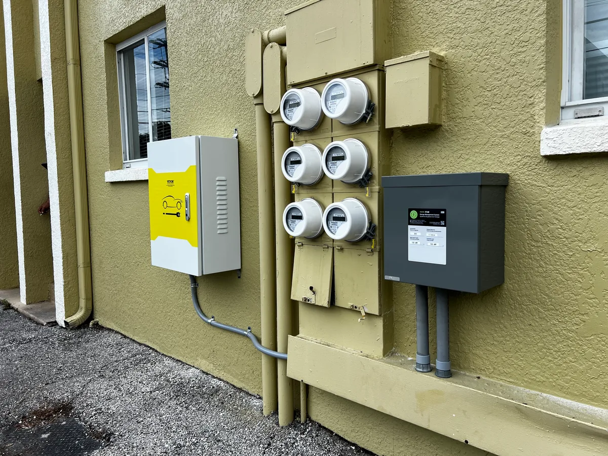 EV load management controller beside a six-gang meter stack on a multi-unit building, installed by Far Out Design in Tampa Bay