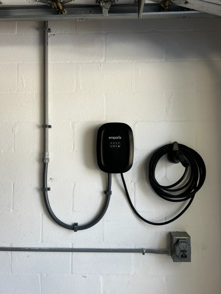 Level 2 EV charger hardwired on a garage wall with conduit, coiled charging cable and a disconnect, installed by Far Out Design in Tampa Bay
