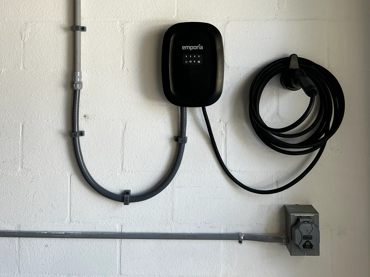 Level 2 EV charger hardwired on a garage wall with conduit, coiled charging cable and a disconnect, installed by Far Out Design in Tampa Bay