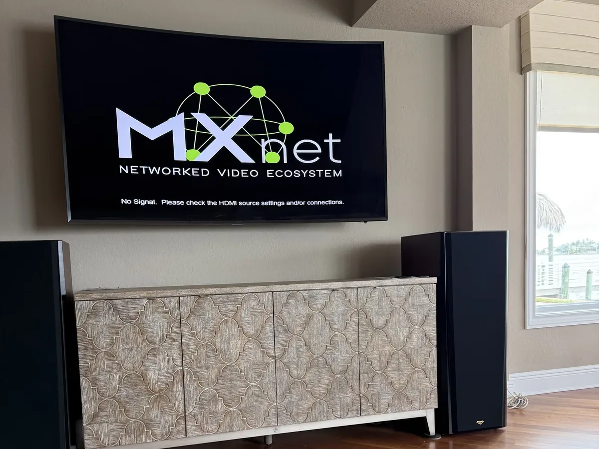 Wall-mounted display running the MXnet networked video system above a media console and floorstanding speakers — IP video and audio distribution by Far Out Design, Pinellas County FL