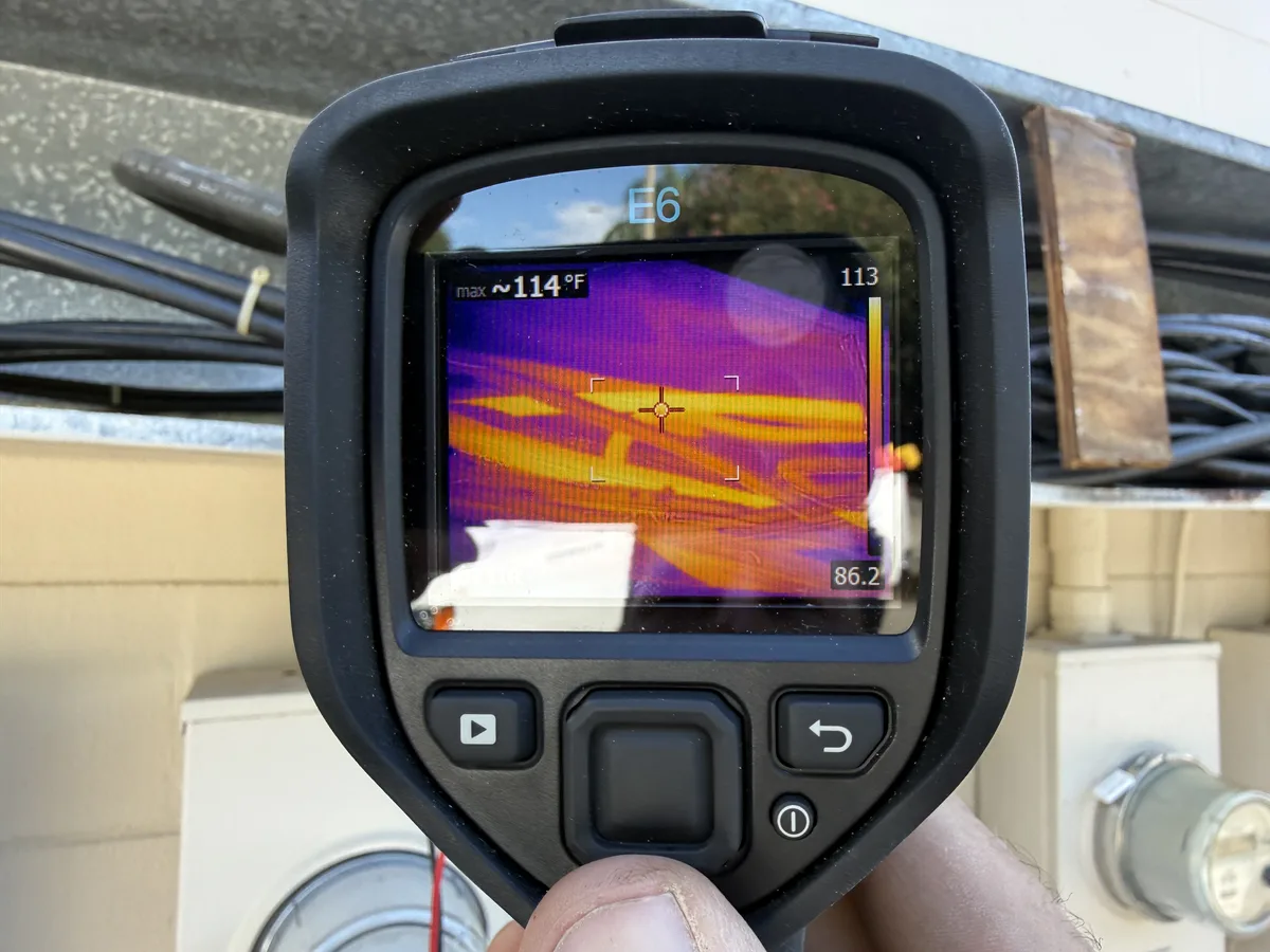 Thermal camera scanning the service cables above an outdoor meter bank, reading about 114 degrees Fahrenheit