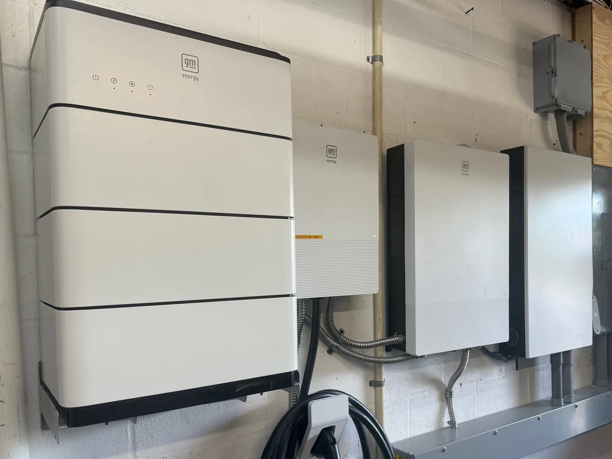Wall-mounted home battery stack with inverter and hub units and an EV connector, installed in a garage — battery backup and grid-tie system by Far Out Design